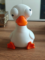 Small goose desk figure with movable eyes styled on a wooden shelf next to a plant
