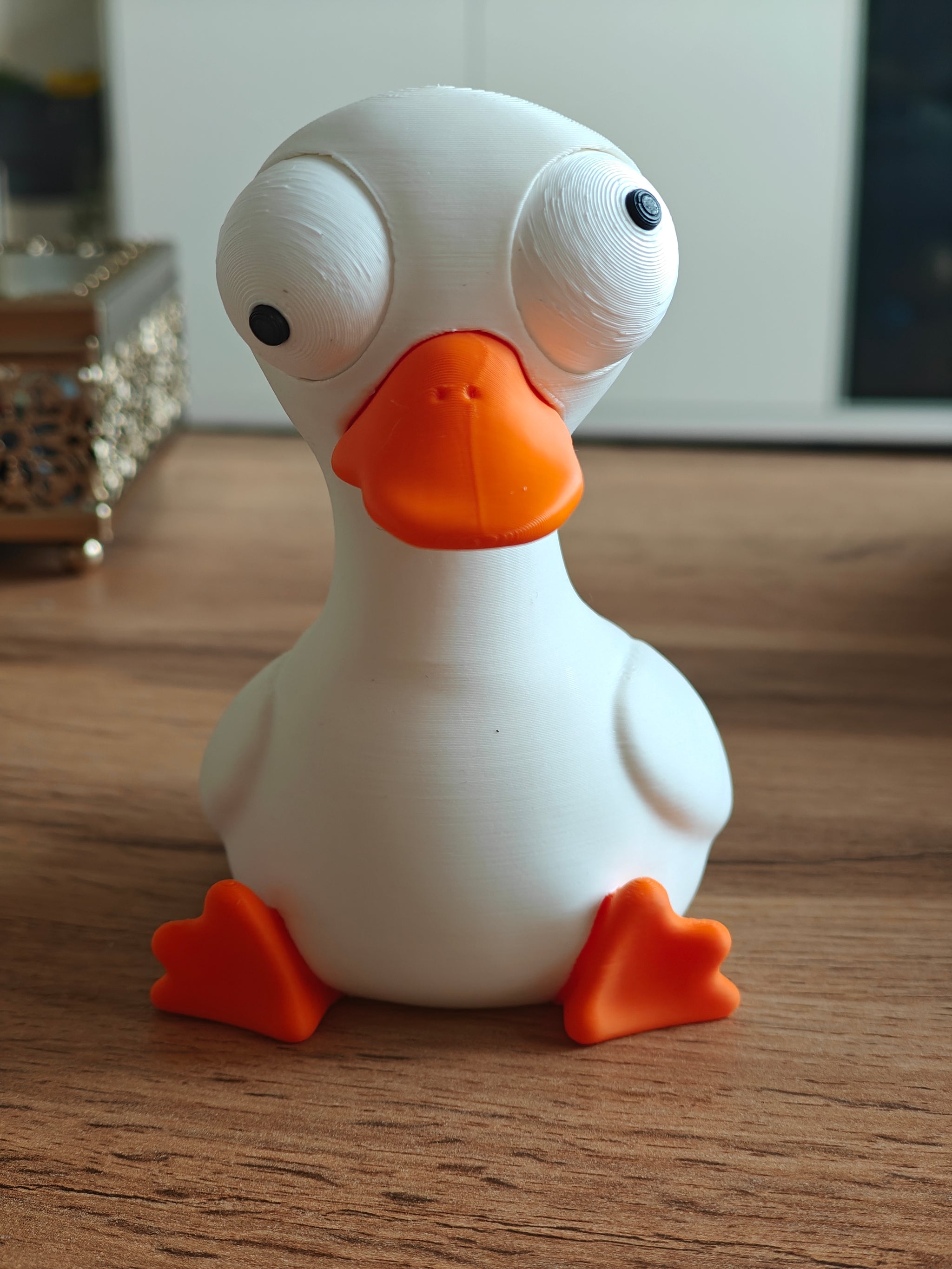 Small goose desk figure with movable eyes styled on a wooden shelf next to a plant