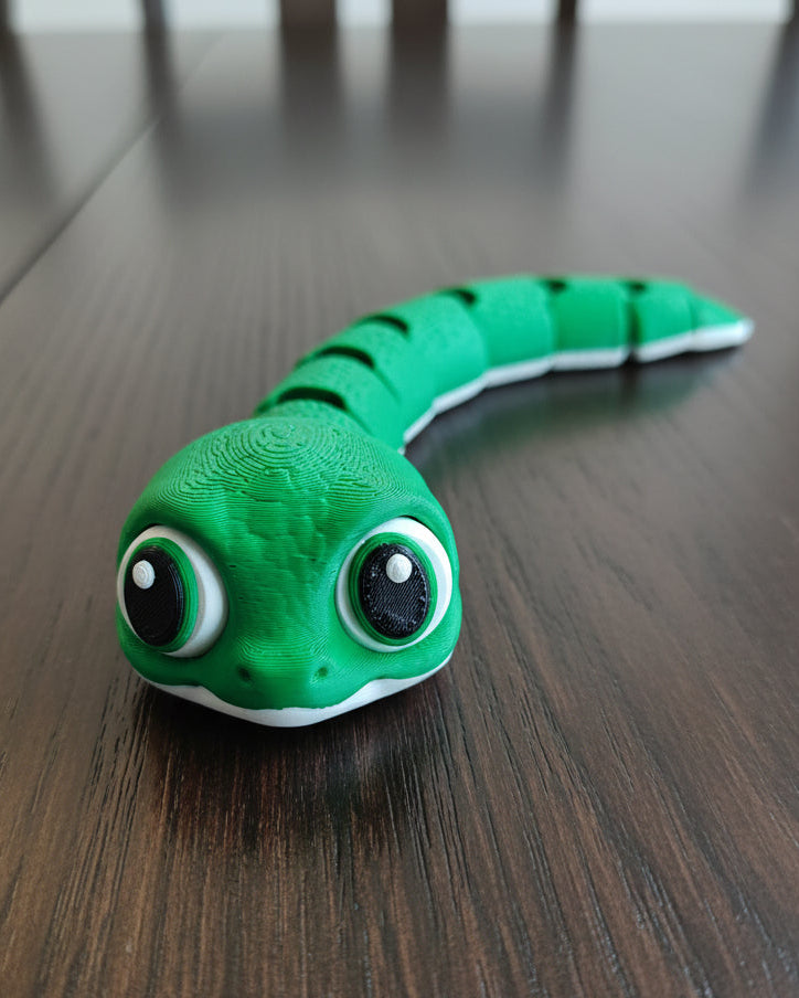 Flexi baby snake figure posed on a wooden desk next to a small plant