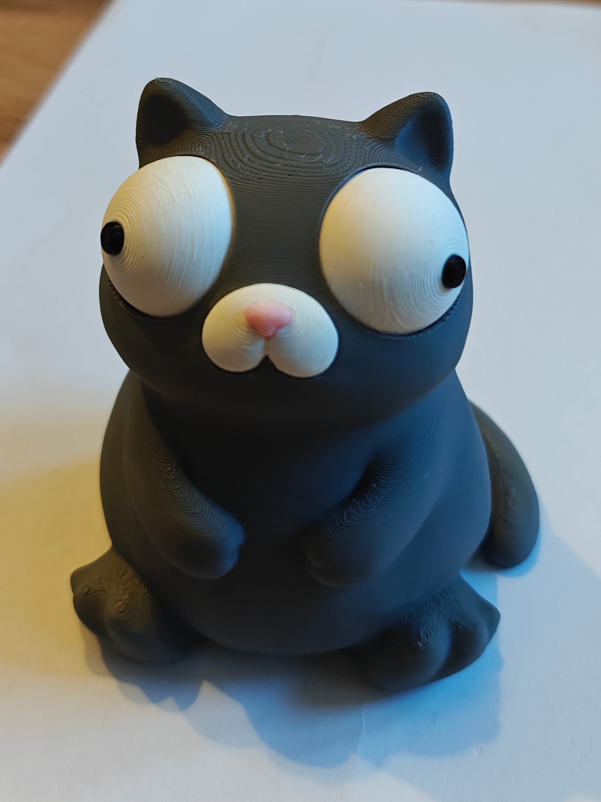 Close-up of a chunky white cat figure with large movable googly eyes on a light surface