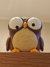 Cartoon owl figure sitting on a wooden desk next to a small plant