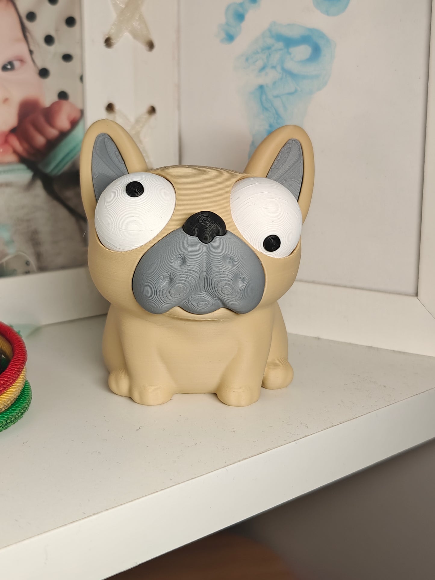 Goofy Frenchie bulldog figure sitting on a wooden desk next to a keyboard and plant