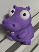 Goofy hippo figure with movable eyes sitting on a wooden desk next to a coffee cup