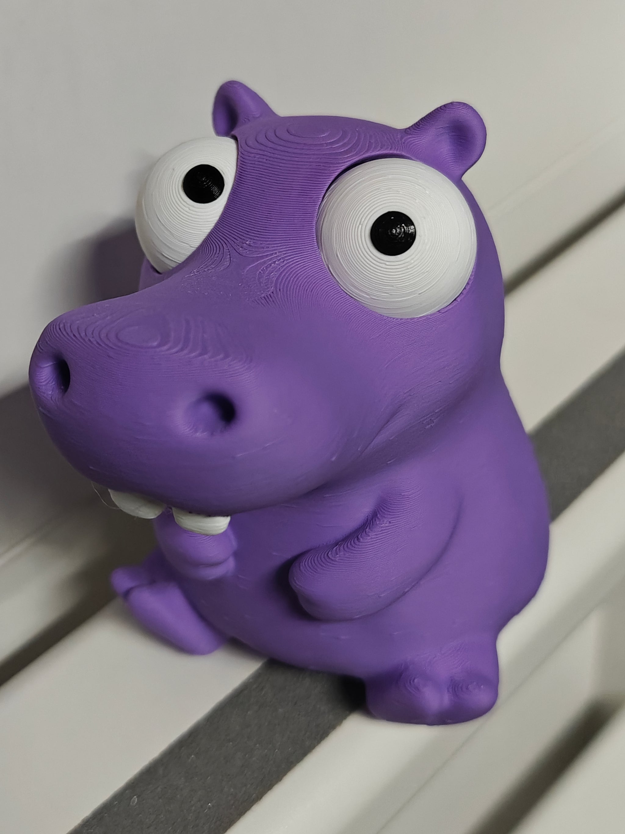 Goofy hippo figure with movable eyes sitting on a wooden desk next to a coffee cup