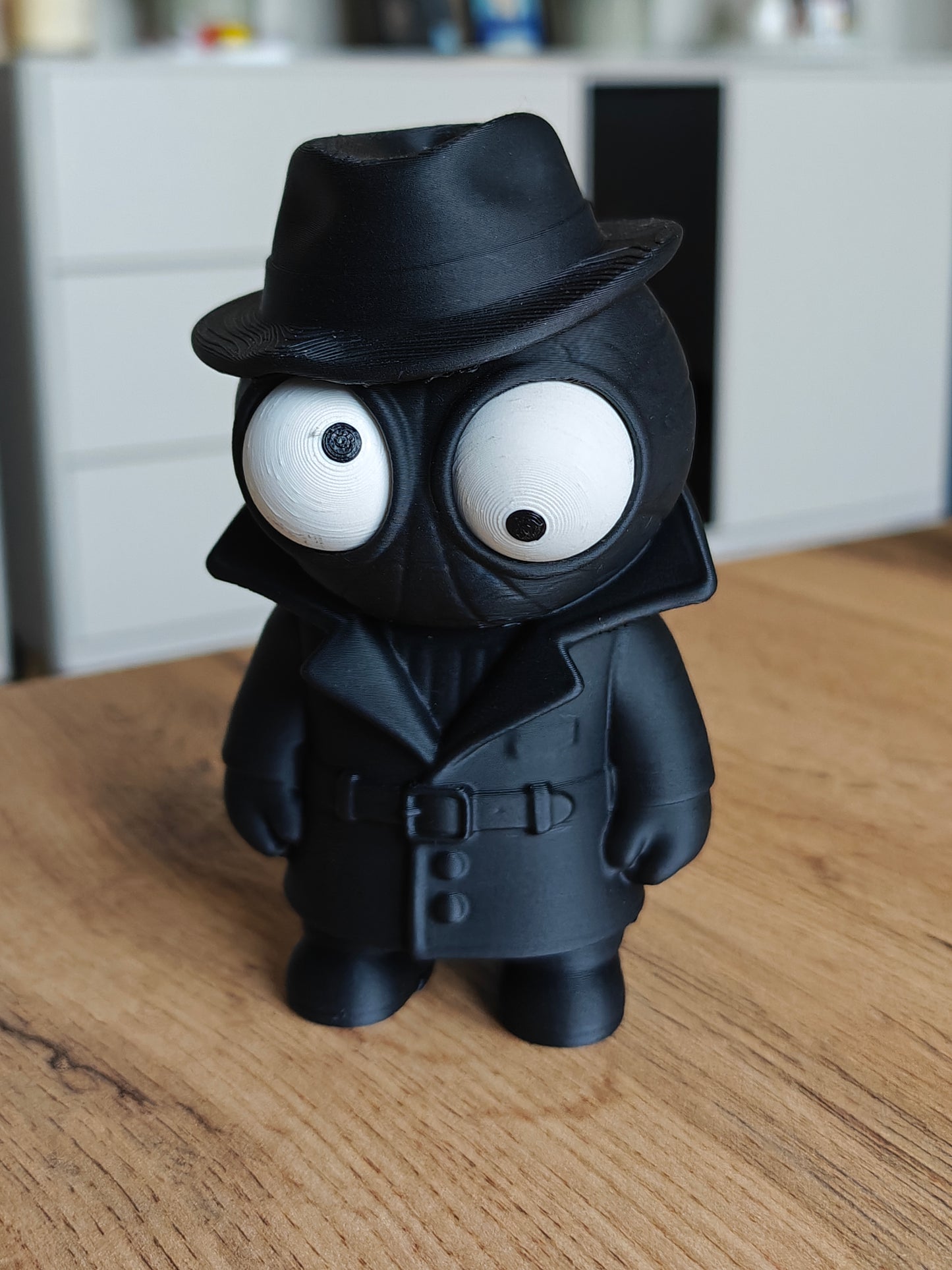 Spider Noir googly eyes figure with dark coat and hat, close-up on white background