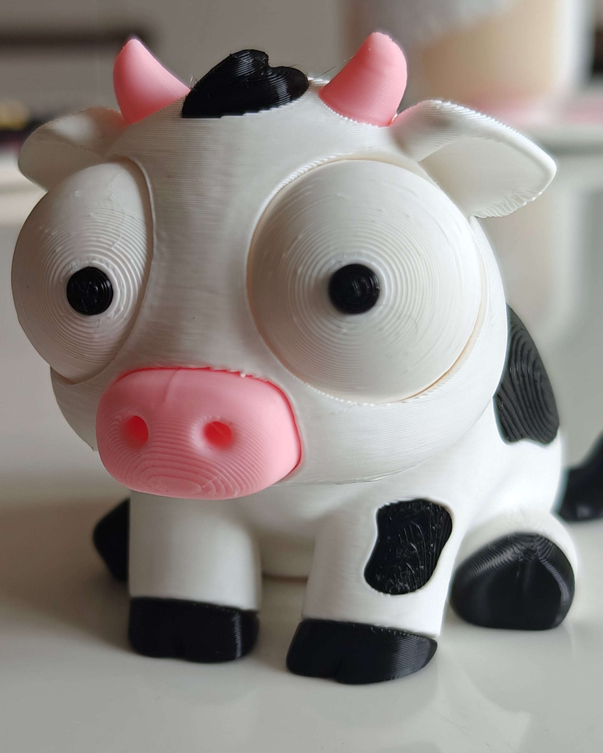 Close-up of goofy cow figure with large movable googly eyes, white and black character on plain background