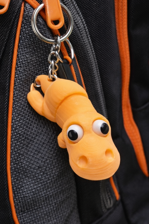 Bright orange 3D-printed dinosaur keychain with googly eyes and metal ring attachment