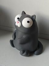 Goofy cat figure with movable eyes sitting on a wooden desk next to a coffee mug