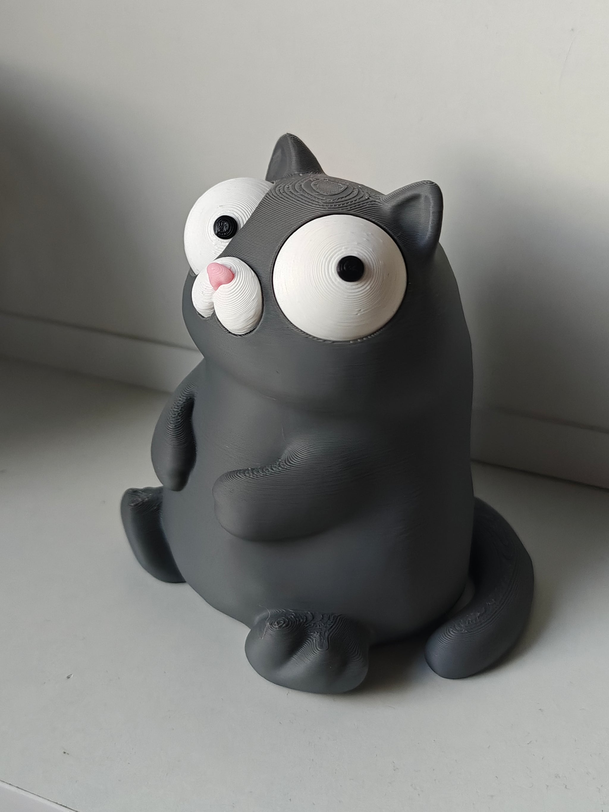 Goofy cat figure with movable eyes sitting on a wooden desk next to a coffee mug