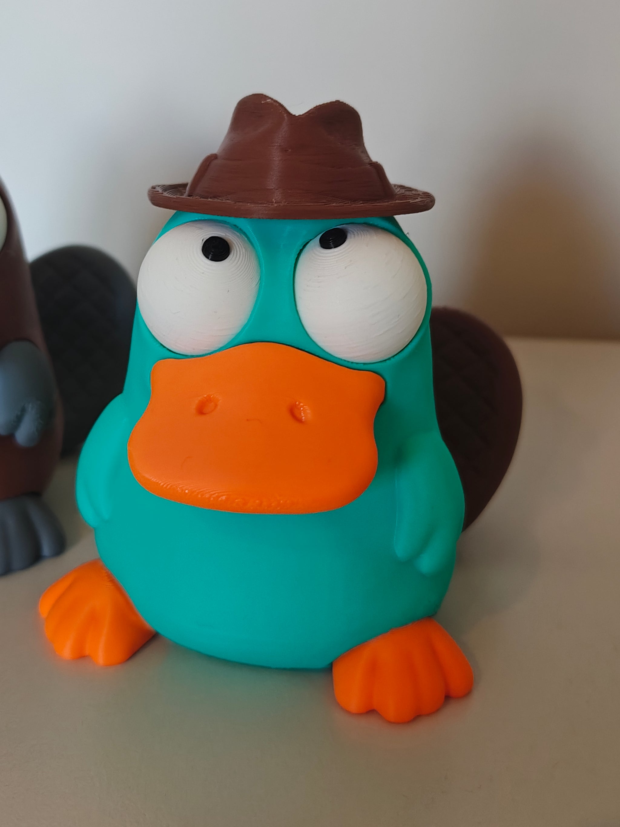 Platypus figure with movable eyes sitting on a wooden desk next to a coffee cup