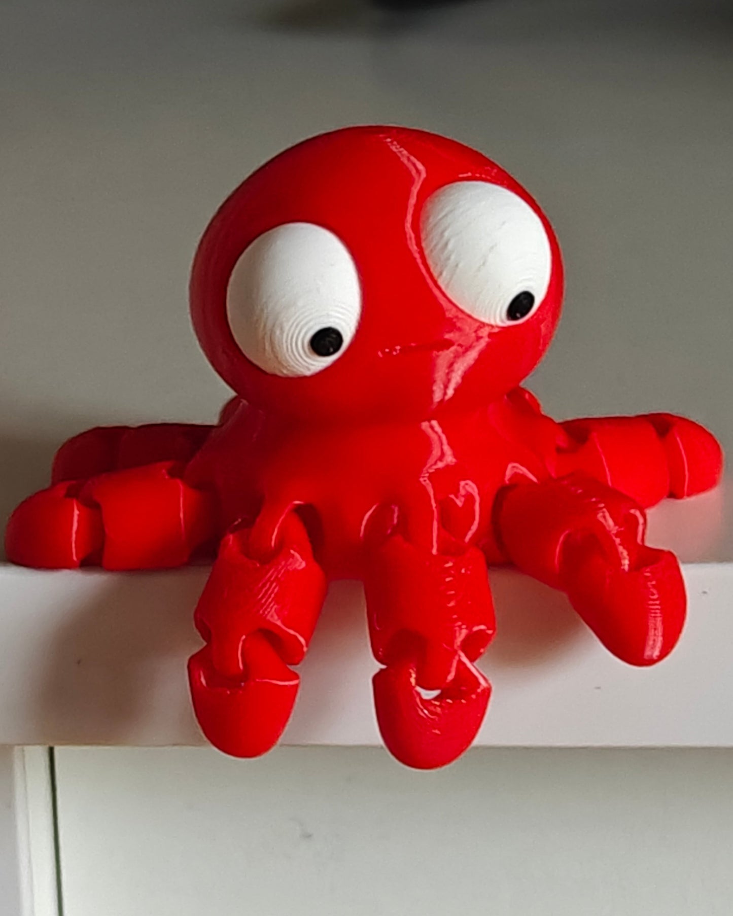 Small flexi octopus with big googly eyes sitting on a wooden desk next to a coffee cup