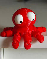 Small flexi octopus with big googly eyes sitting on a wooden desk next to a coffee cup