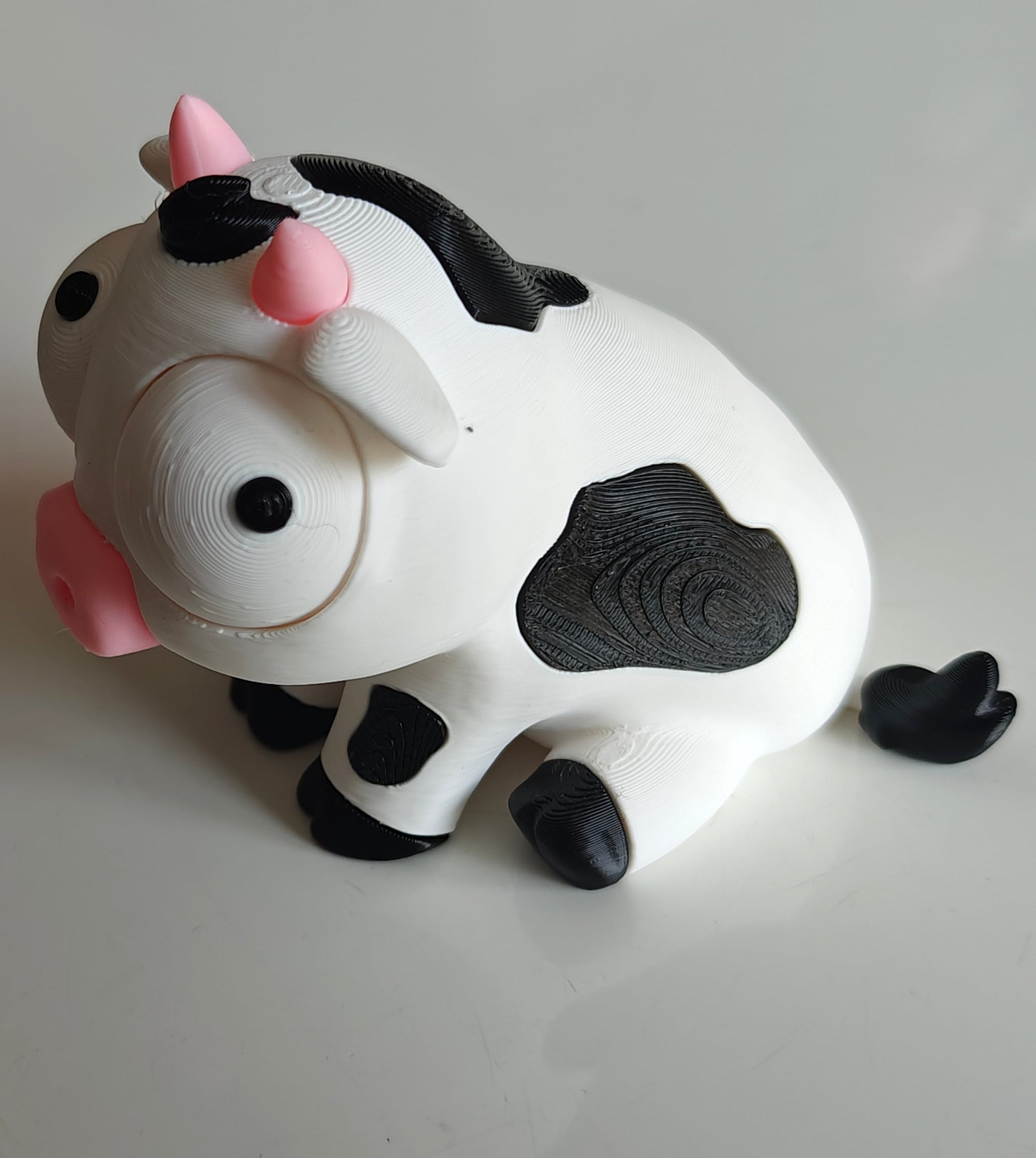 Close-up of goofy cow figure with large movable googly eyes, white and black character on plain background