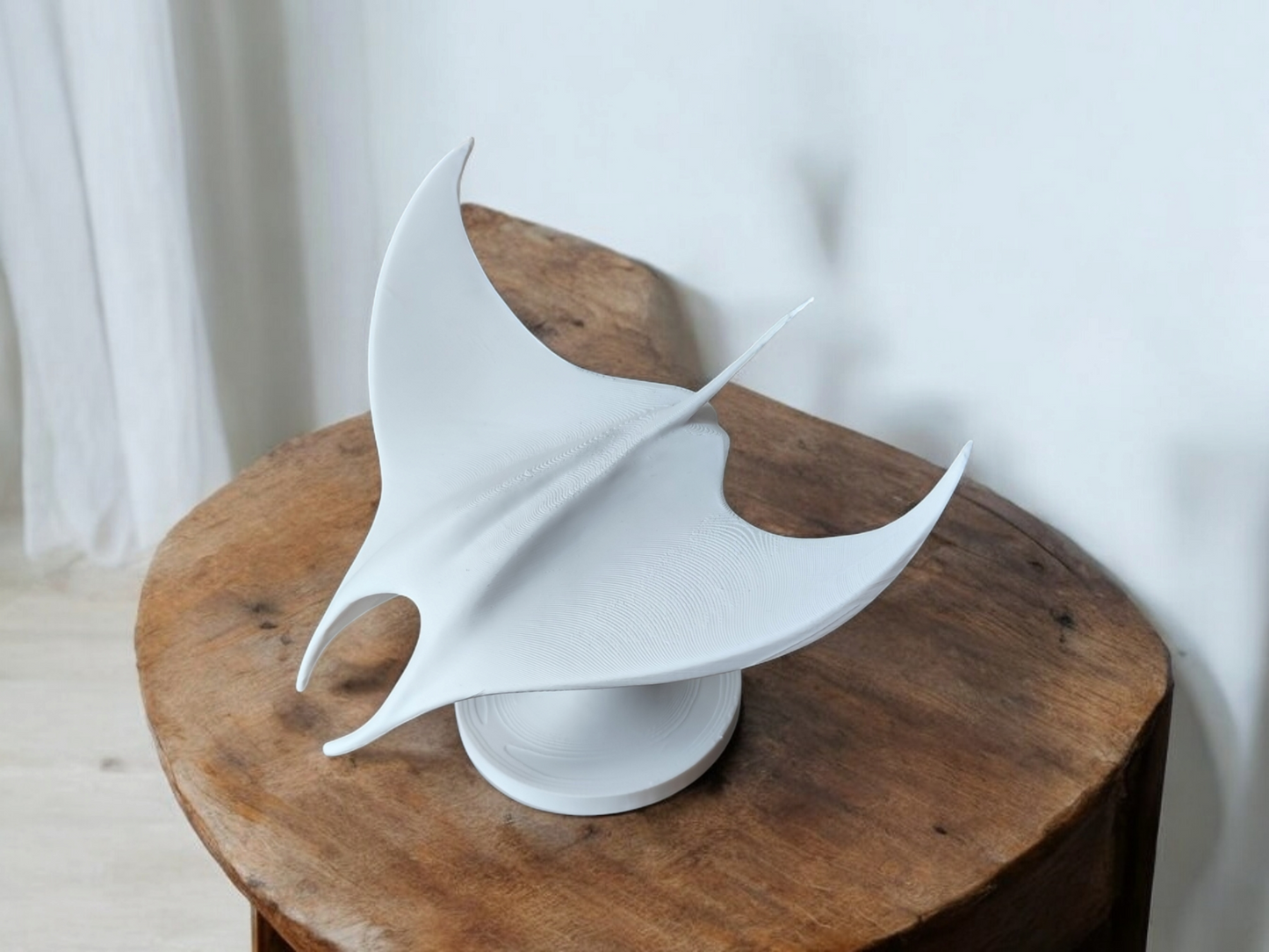 Minimalist manta ray sculpture displayed on a light wooden shelf against a white wall