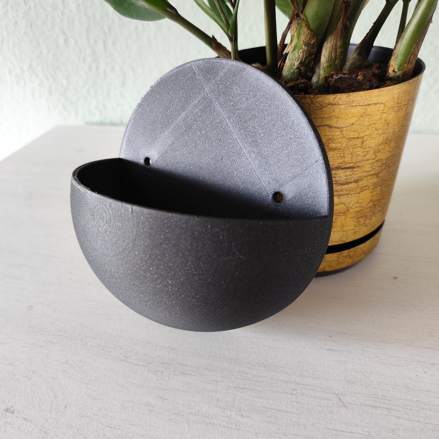 Wall-mounted ball plant pot displayed in a living room corner with trailing green plant