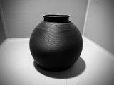 Minimalist round vase on wooden shelf with single dried flower stem