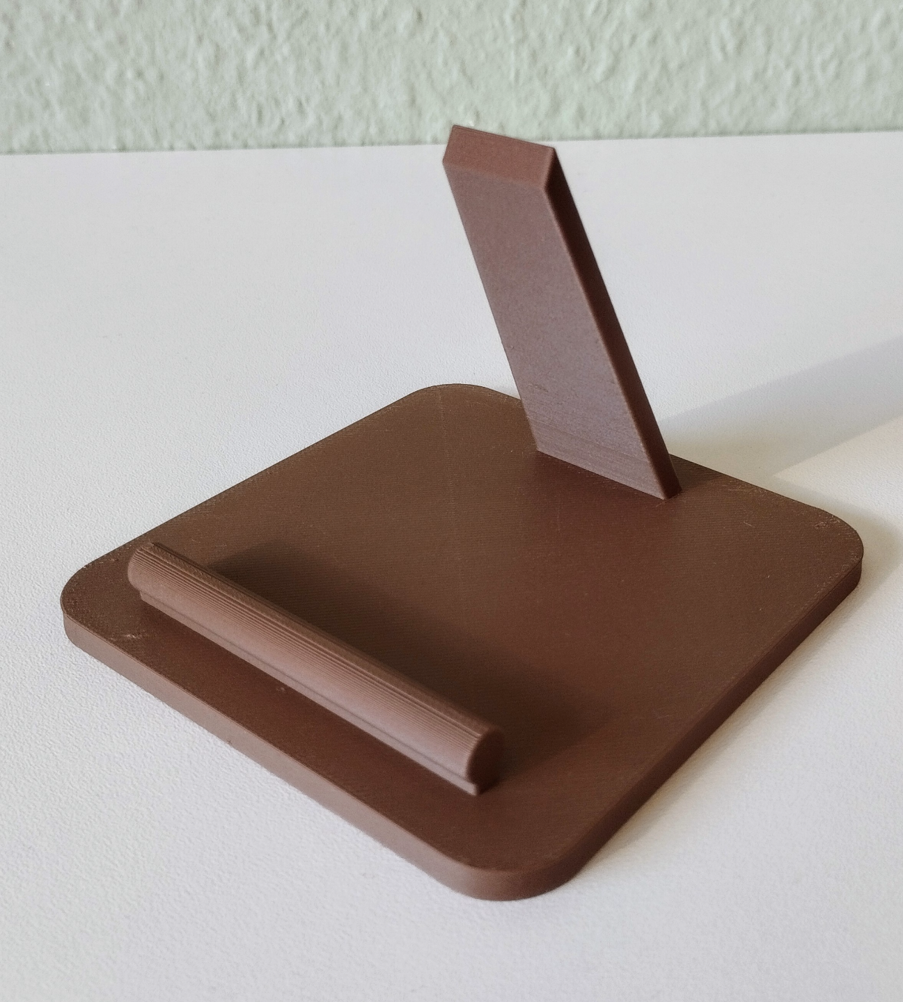Smartphone stand on a desk beside a lamp and notebook, phone displayed at viewing angle