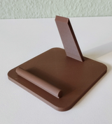 Smartphone stand on a desk beside a lamp and notebook, phone displayed at viewing angle