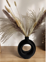Minimalist ring vase with single dried stem displayed on white shelf