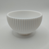Round ribbed bowl displayed on wooden shelf with home decor
