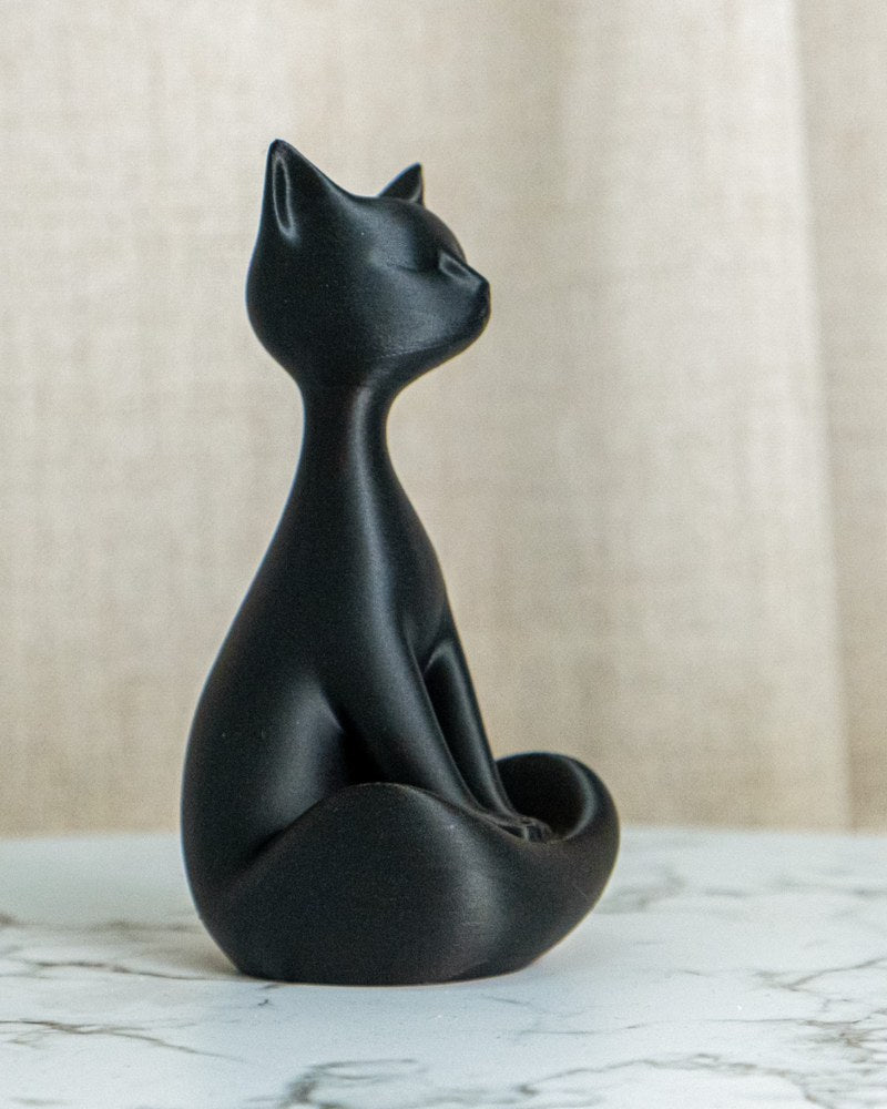 Close-up of a matte black cat sculpture sitting upright against a white background