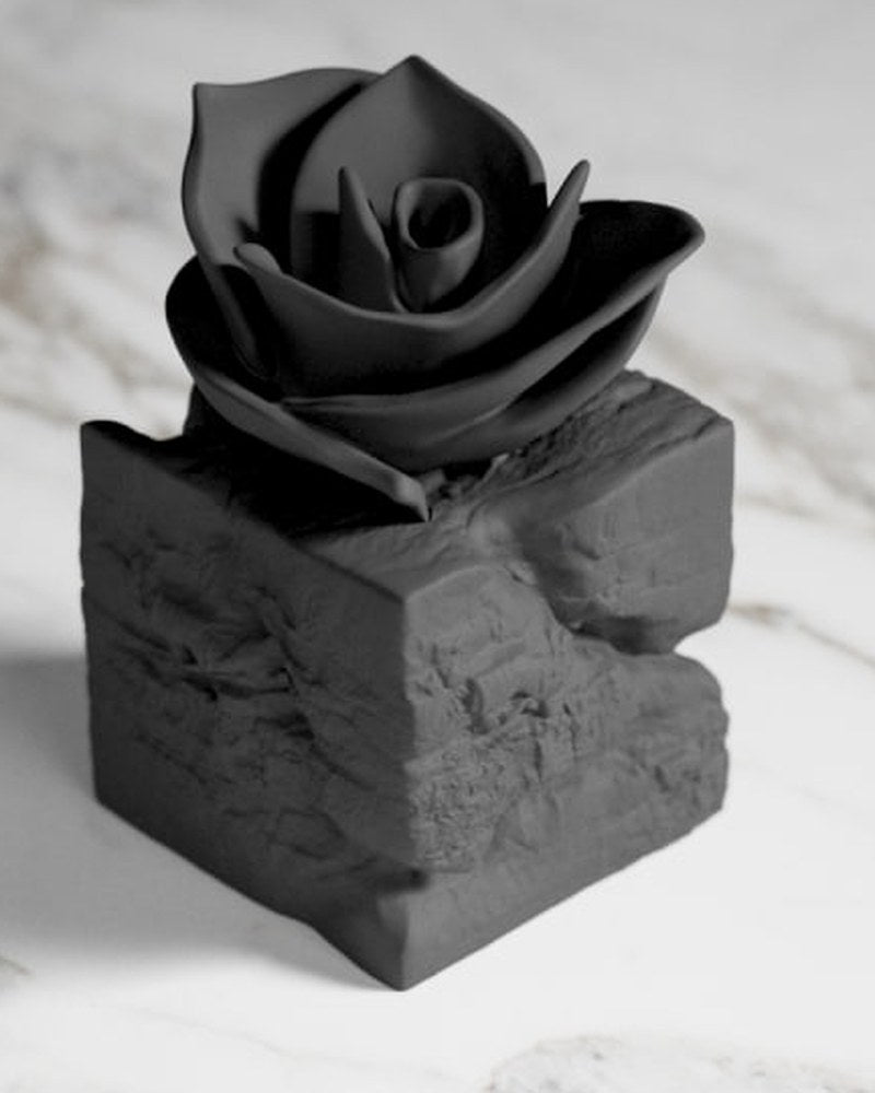 Black rose sculpture emerging from rough stone base, front view on white surface