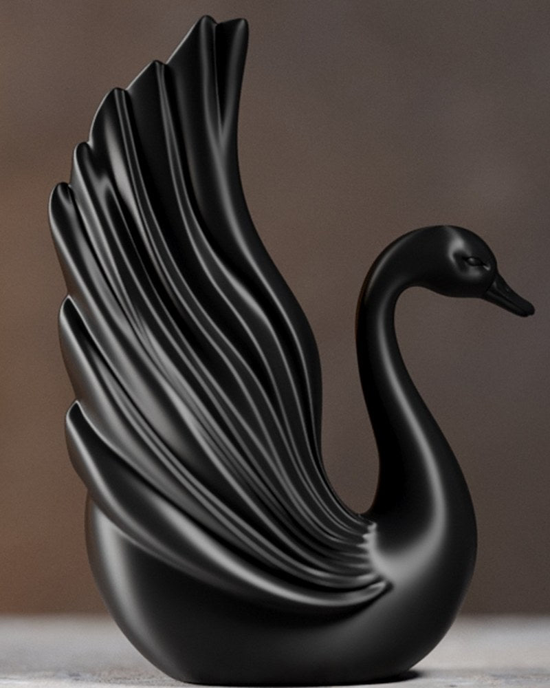 Black swan sculpture with curved neck and lifted wings against a white background