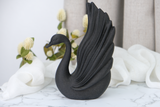 Black swan sculpture styled on a minimalist shelf beside ceramics and a candle