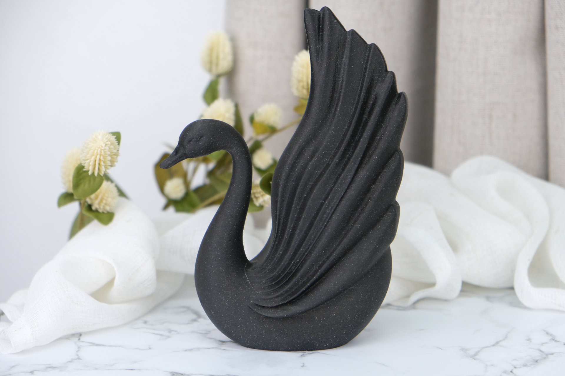 Black swan sculpture styled on a minimalist shelf beside ceramics and a candle