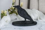 Low poly crow sculpture styled on a wooden shelf with candles and dark ceramics