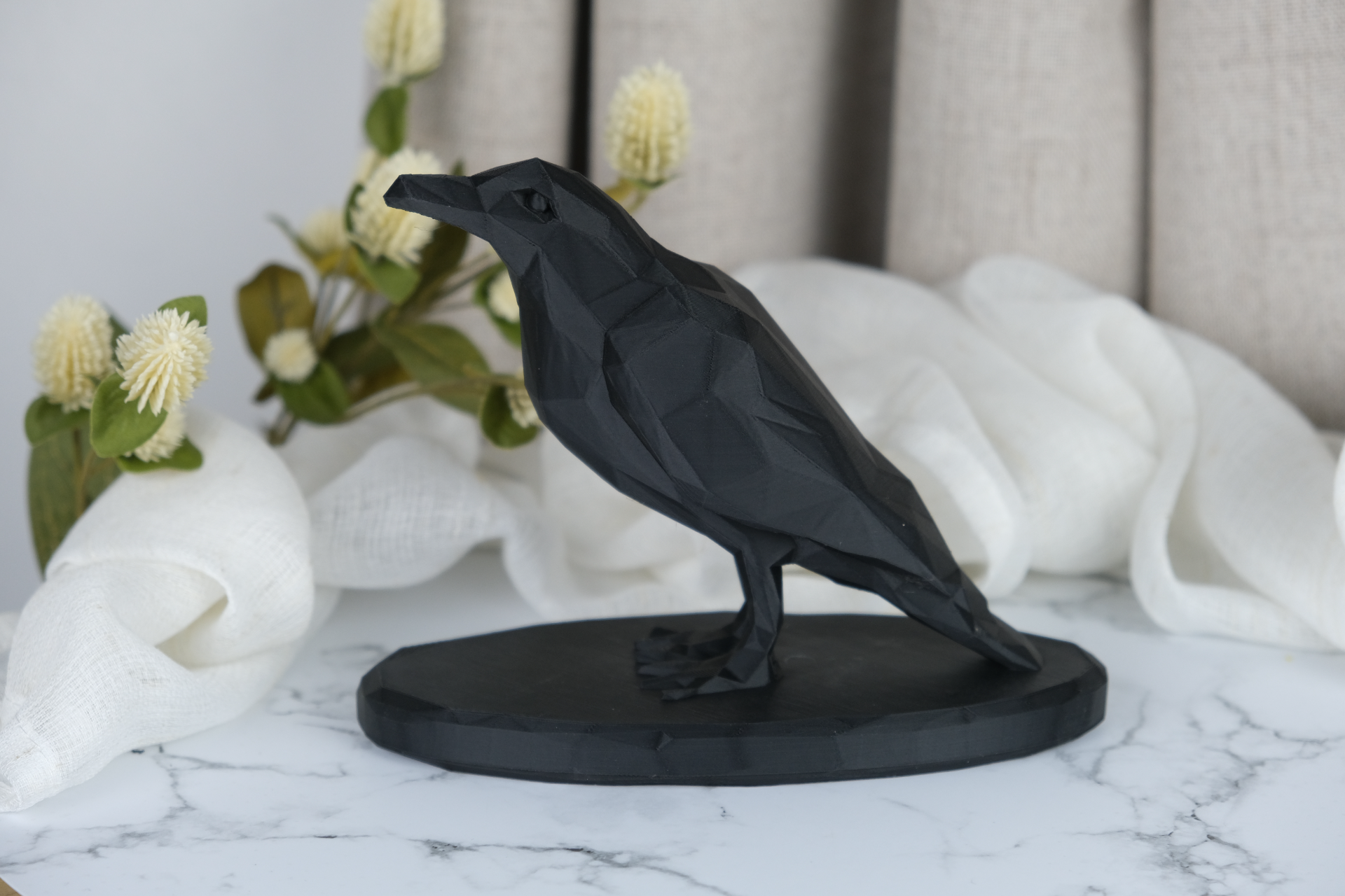 Low poly crow sculpture styled on a wooden shelf with candles and dark ceramics