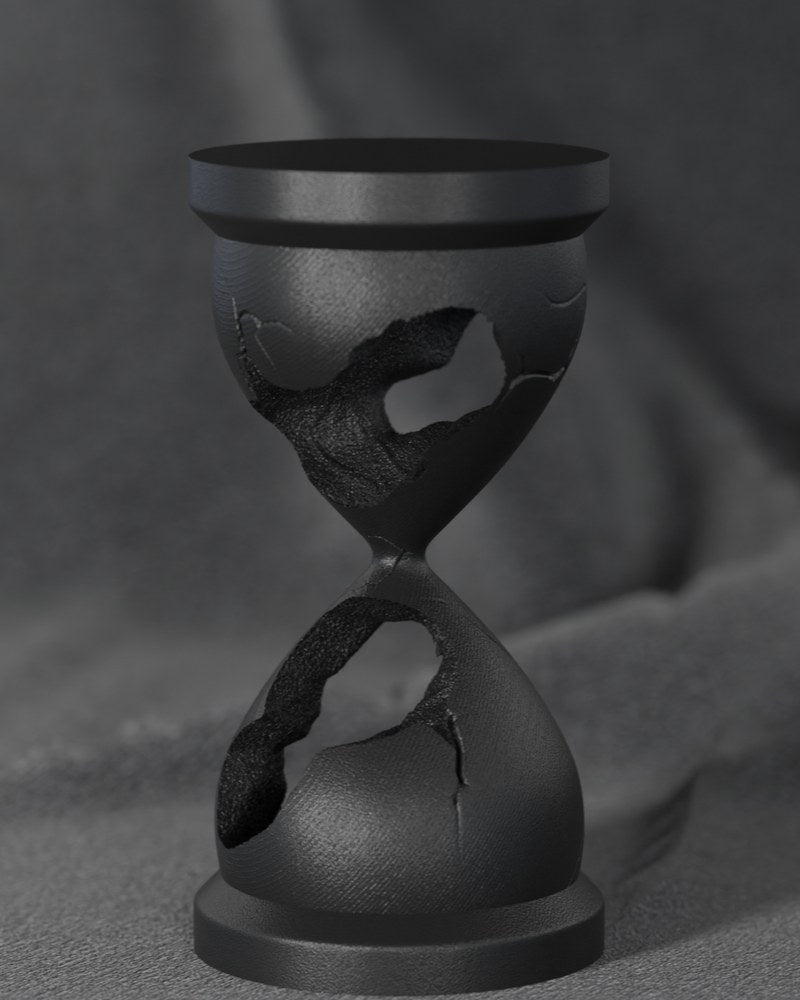 Black broken hourglass sculpture on a white desk — minimalist art sculpture close-up