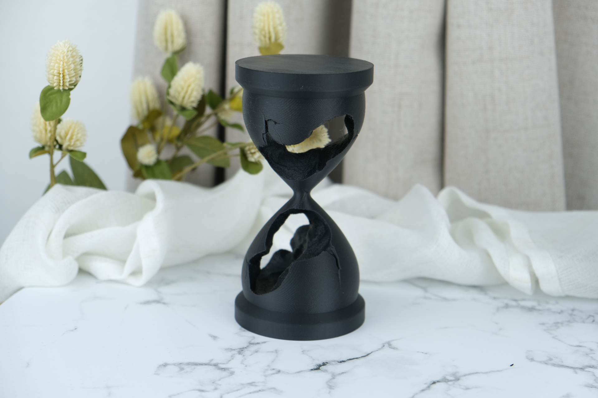 Broken hourglass sculpture styled on a dark shelf with books and abstract objects