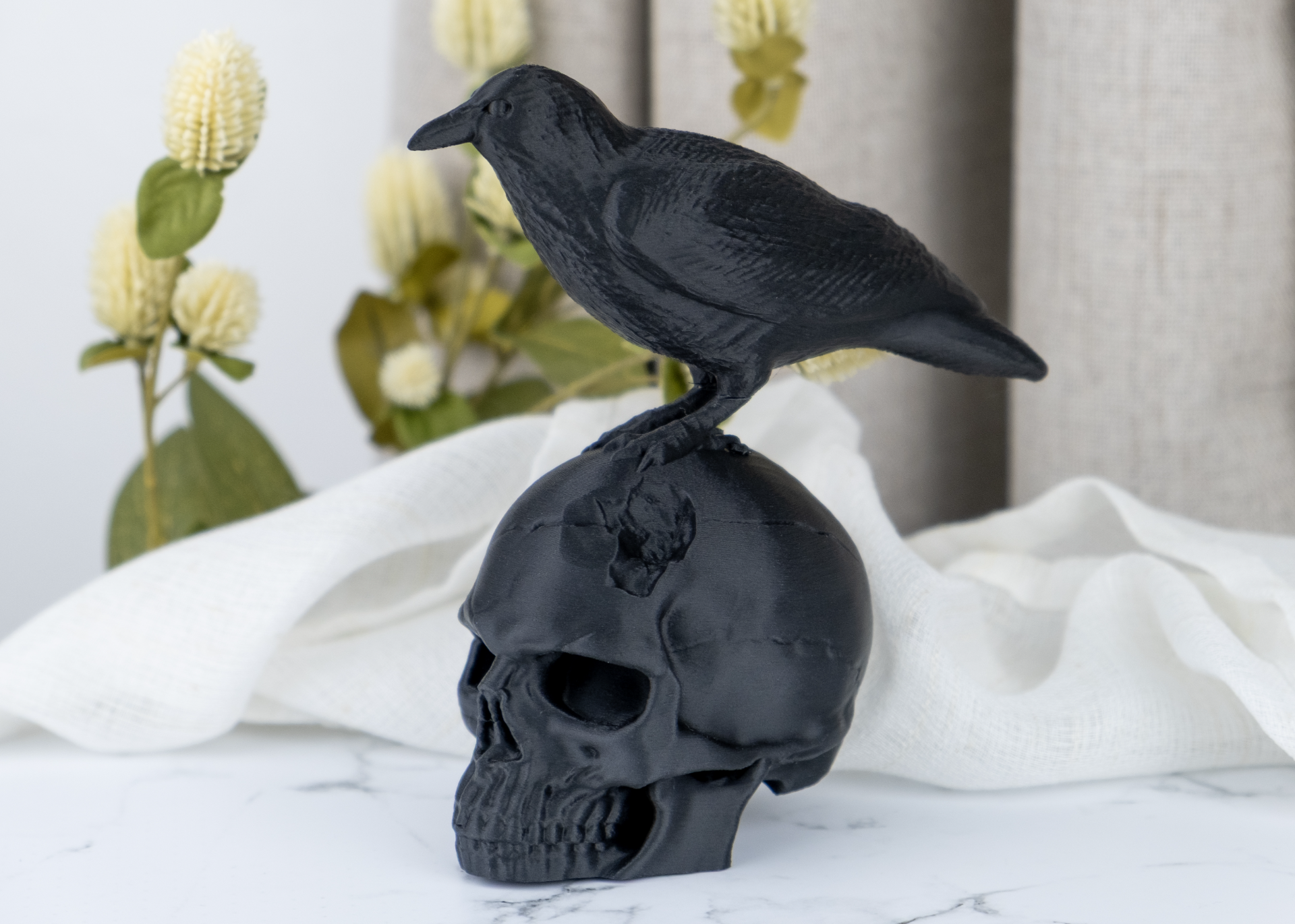 Raven skull sculpture styled on a dark wooden shelf alongside candles and dried botanicals