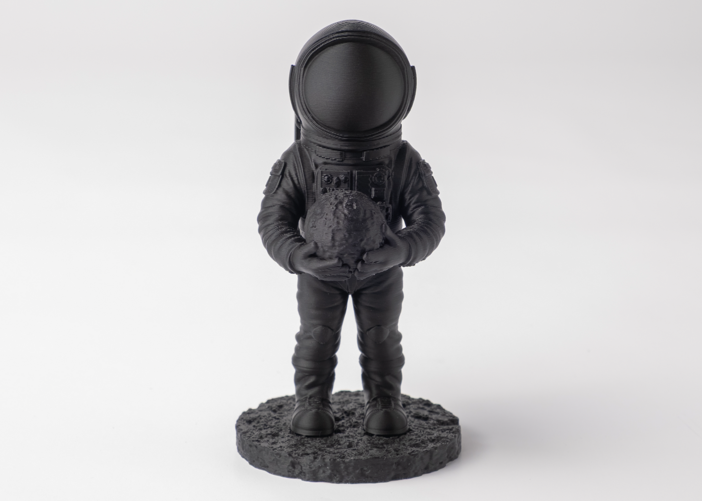 Astronaut sculpture styled on a wooden shelf beside books and a small plant, dark finish
