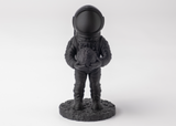 Astronaut sculpture styled on a wooden shelf beside books and a small plant, dark finish