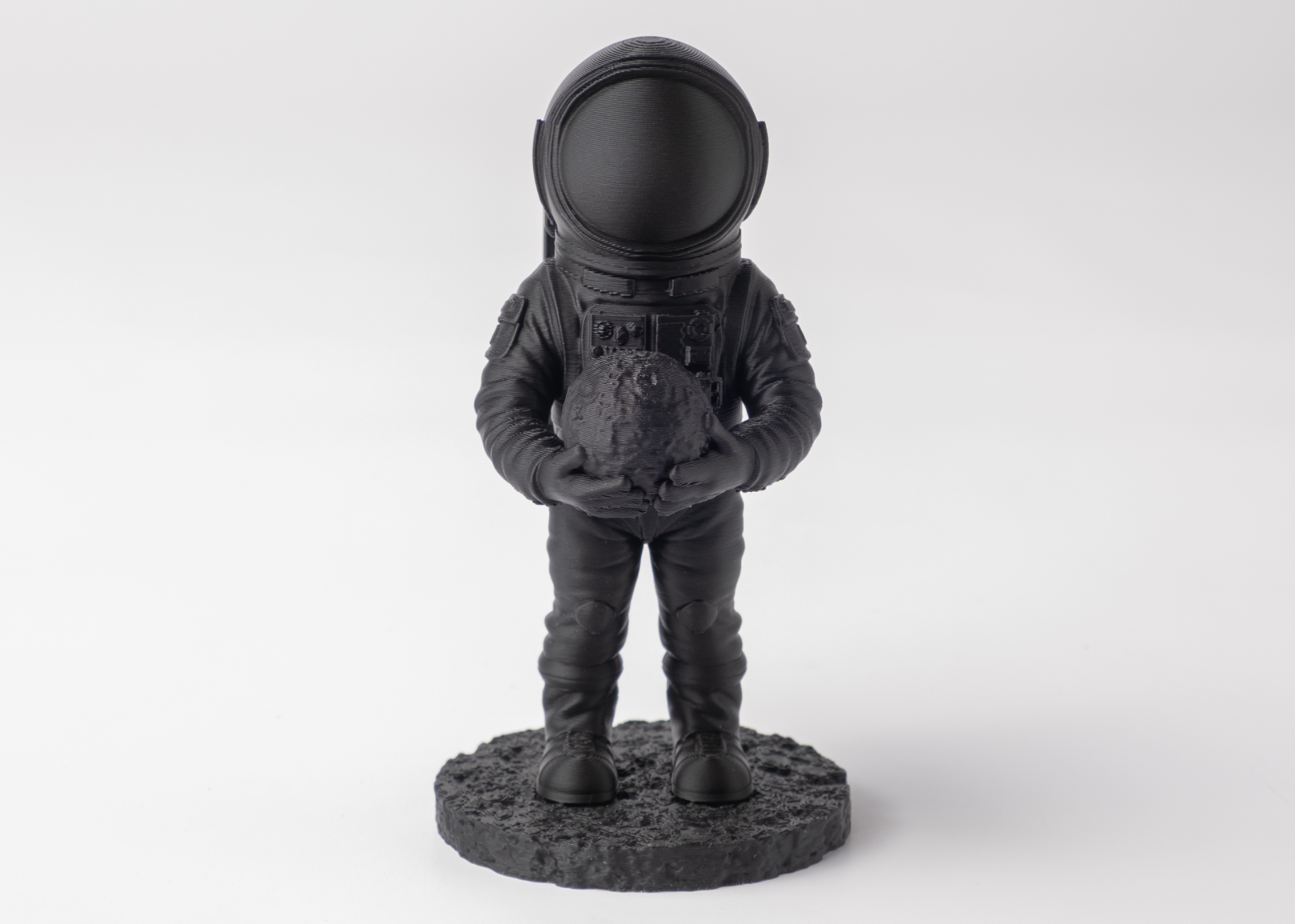 Astronaut sculpture styled on a wooden shelf beside books and a small plant, dark finish