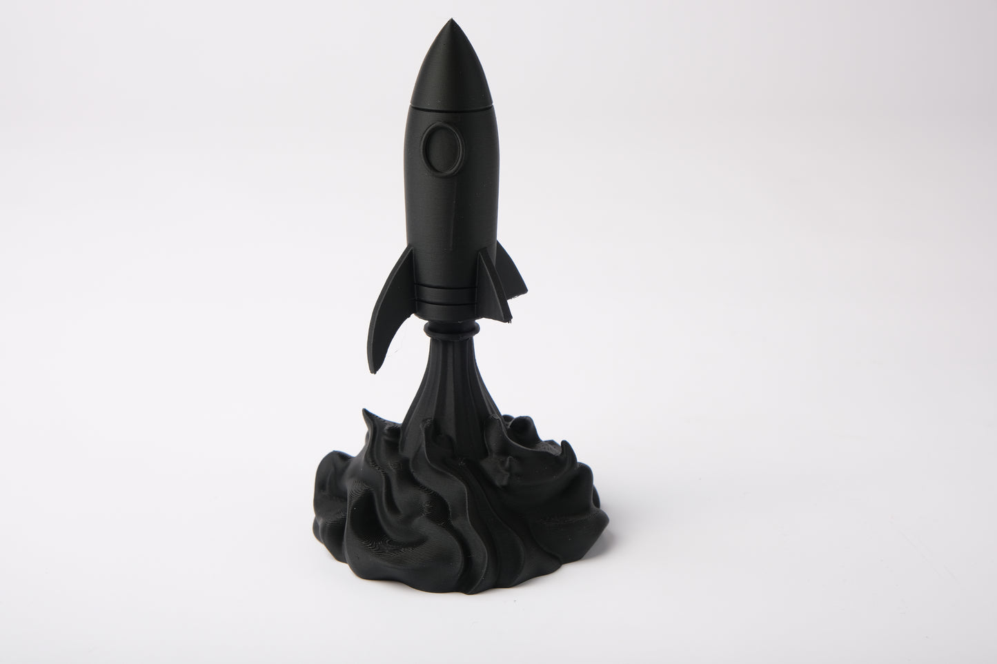 Rocket sculpture styled on a wooden desk alongside books and a small plant in a minimal setting
