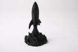 Rocket sculpture styled on a wooden desk alongside books and a small plant in a minimal setting