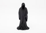 Gothic reaper figure styled on a dark wooden shelf beside a candle and dried botanicals