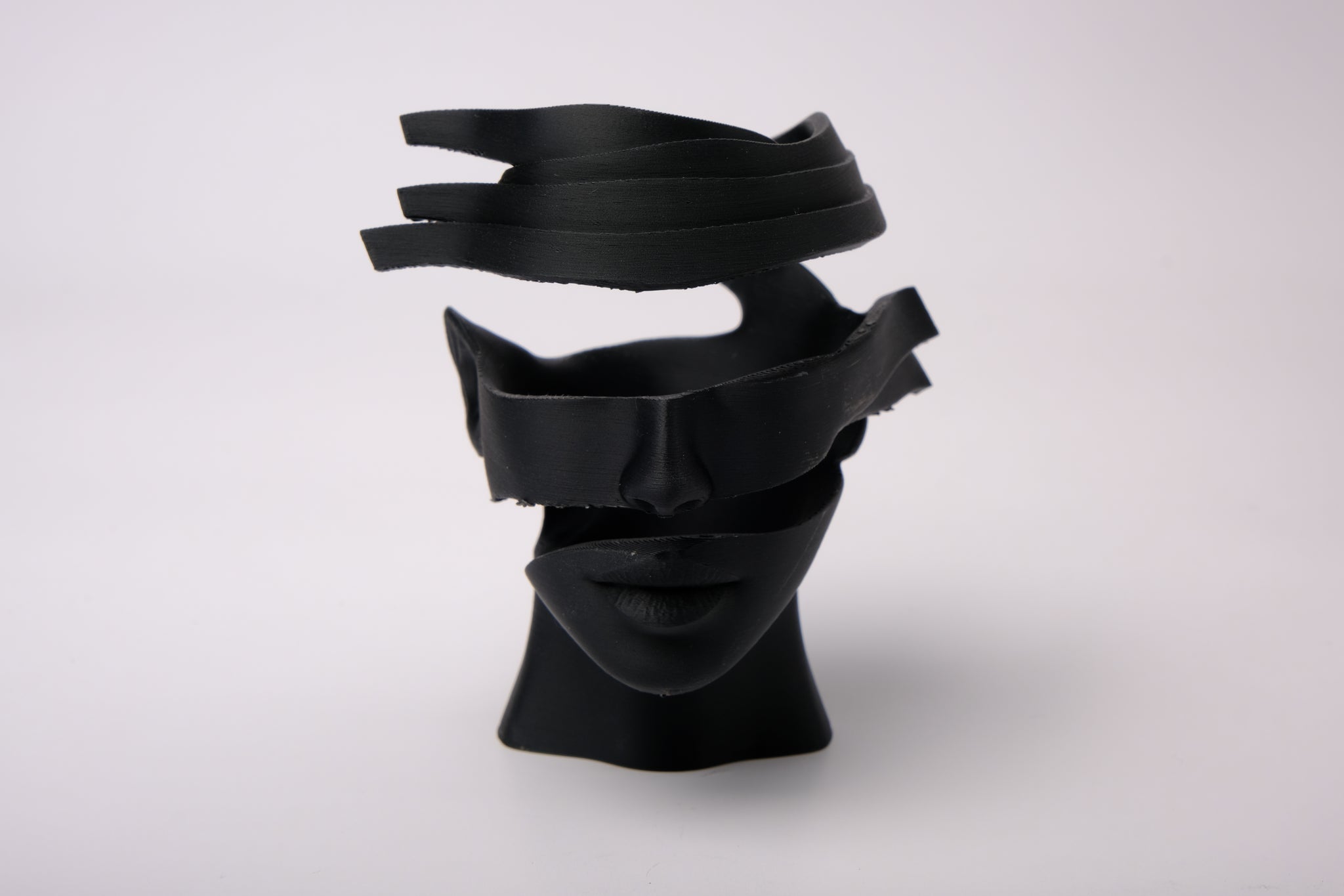 Surreal abstract face sculpture styled on a minimalist shelf with books and plants