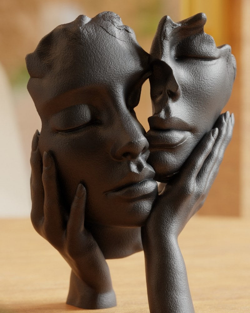 Abstract face sculpture in matte black showing two faces touching, front view on white background