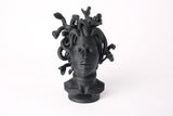 Medusa bust sculpture displayed on a dark wood shelf in a minimalist interior setting