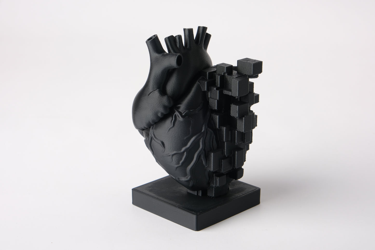 Pixel heart sculpture styled on a wooden desk beside books and a small plant