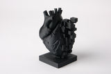 Pixel heart sculpture styled on a wooden desk beside books and a small plant