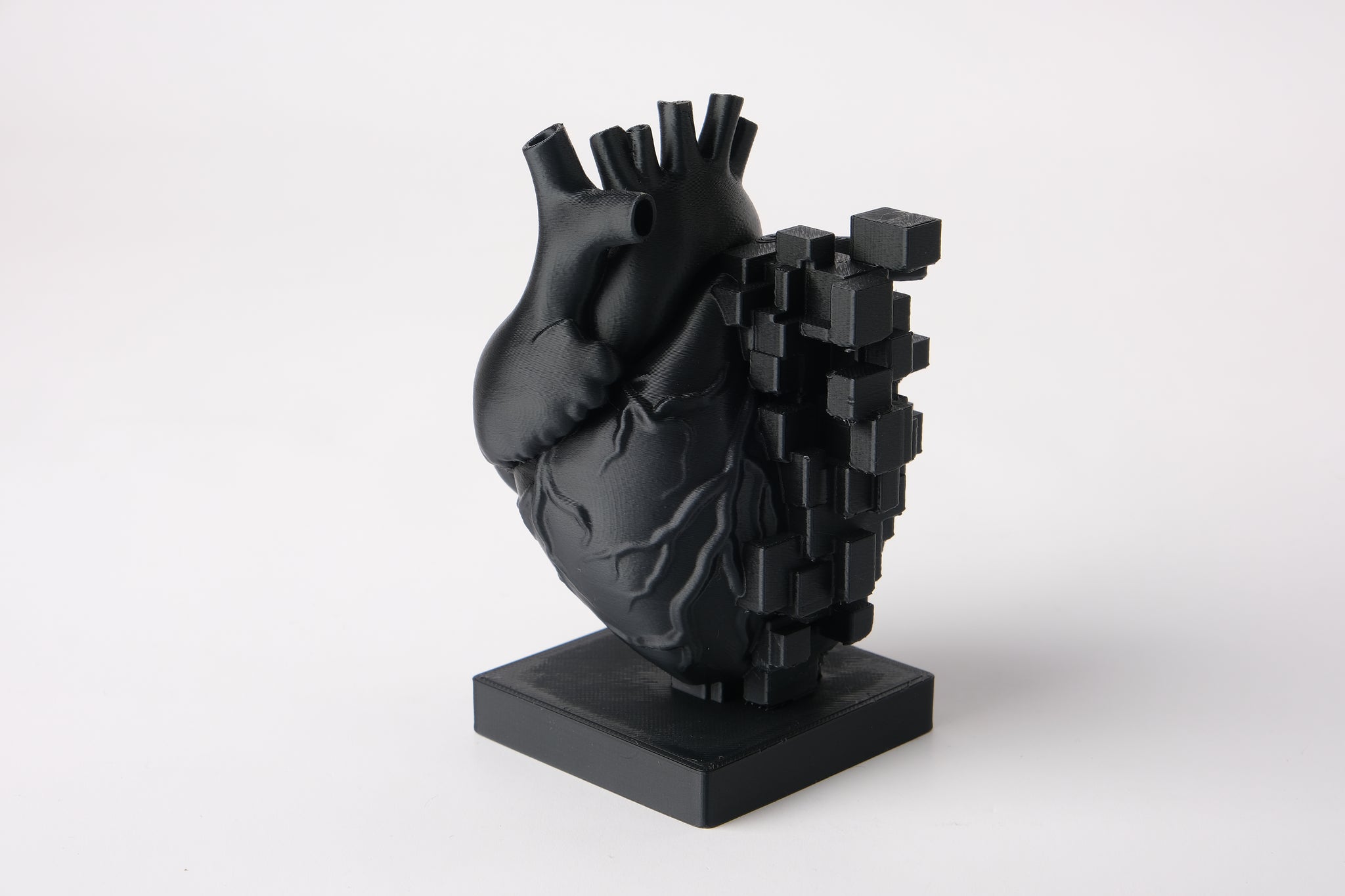 Pixel heart sculpture styled on a wooden desk beside books and a small plant