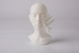 Serenity face sculpture styled on a wooden shelf beside dried botanicals and soft linen
