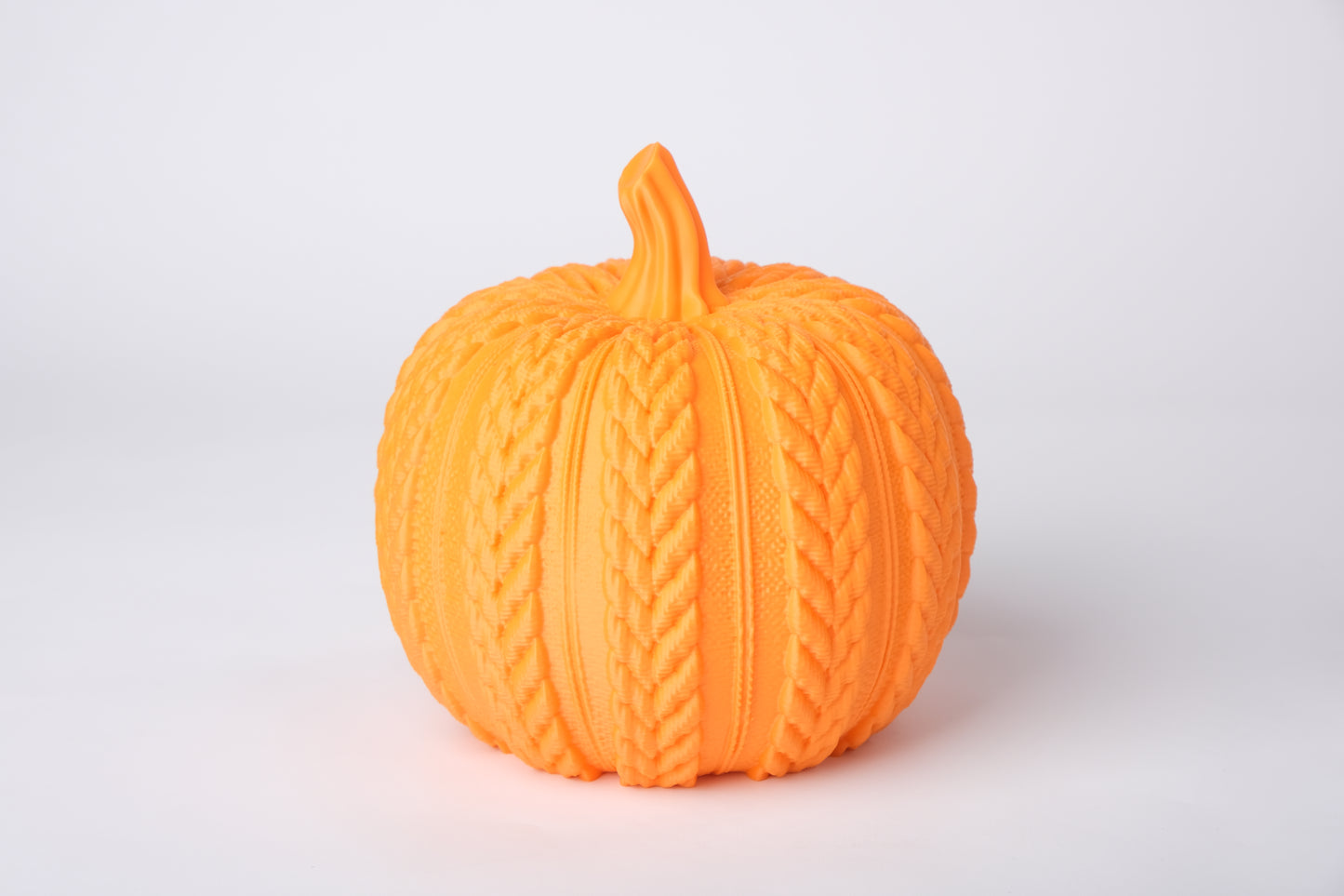 Knitted pumpkin decoration styled on a wooden shelf alongside a lit candle and dried autumn leaves