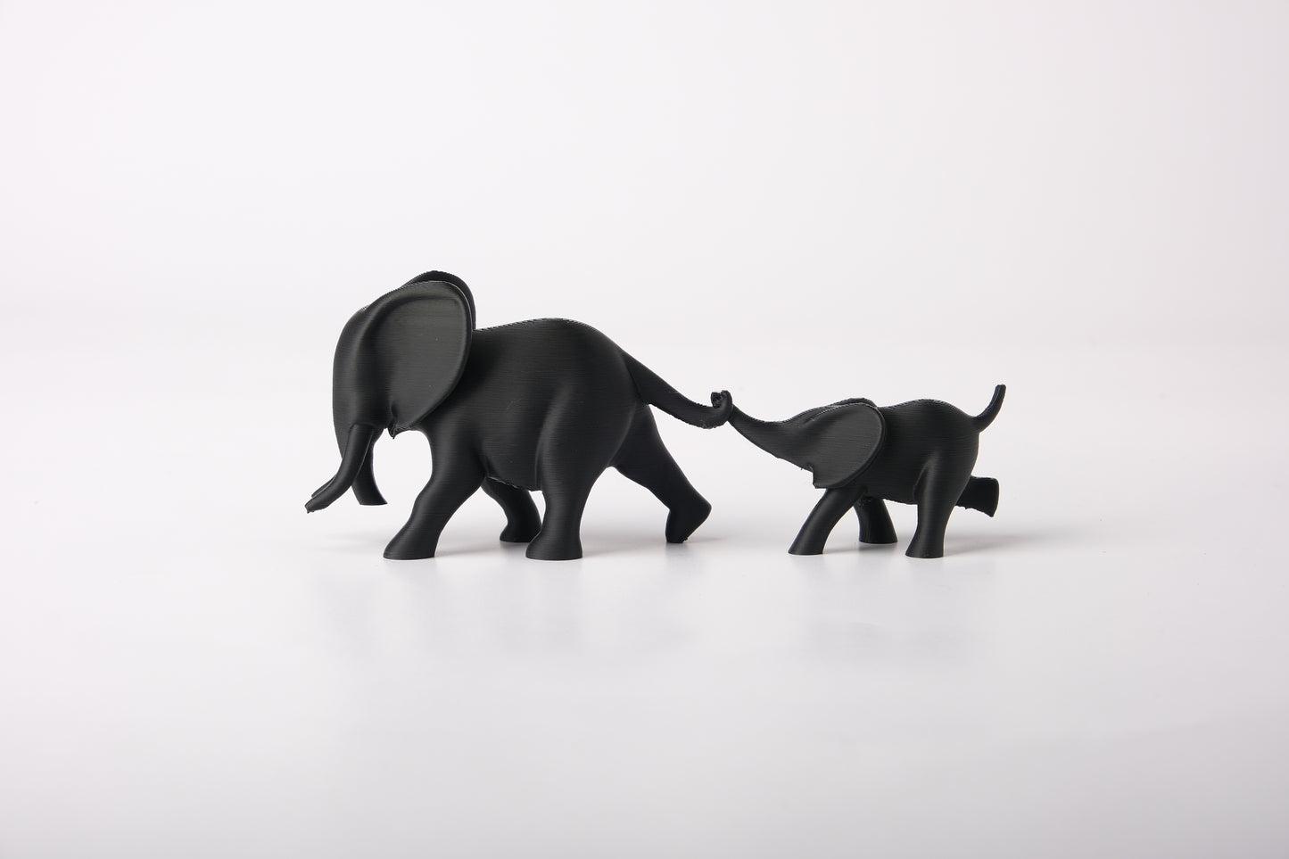 Elephant duo sculpture styled on a wooden shelf next to a small plant and neutral ceramic vase