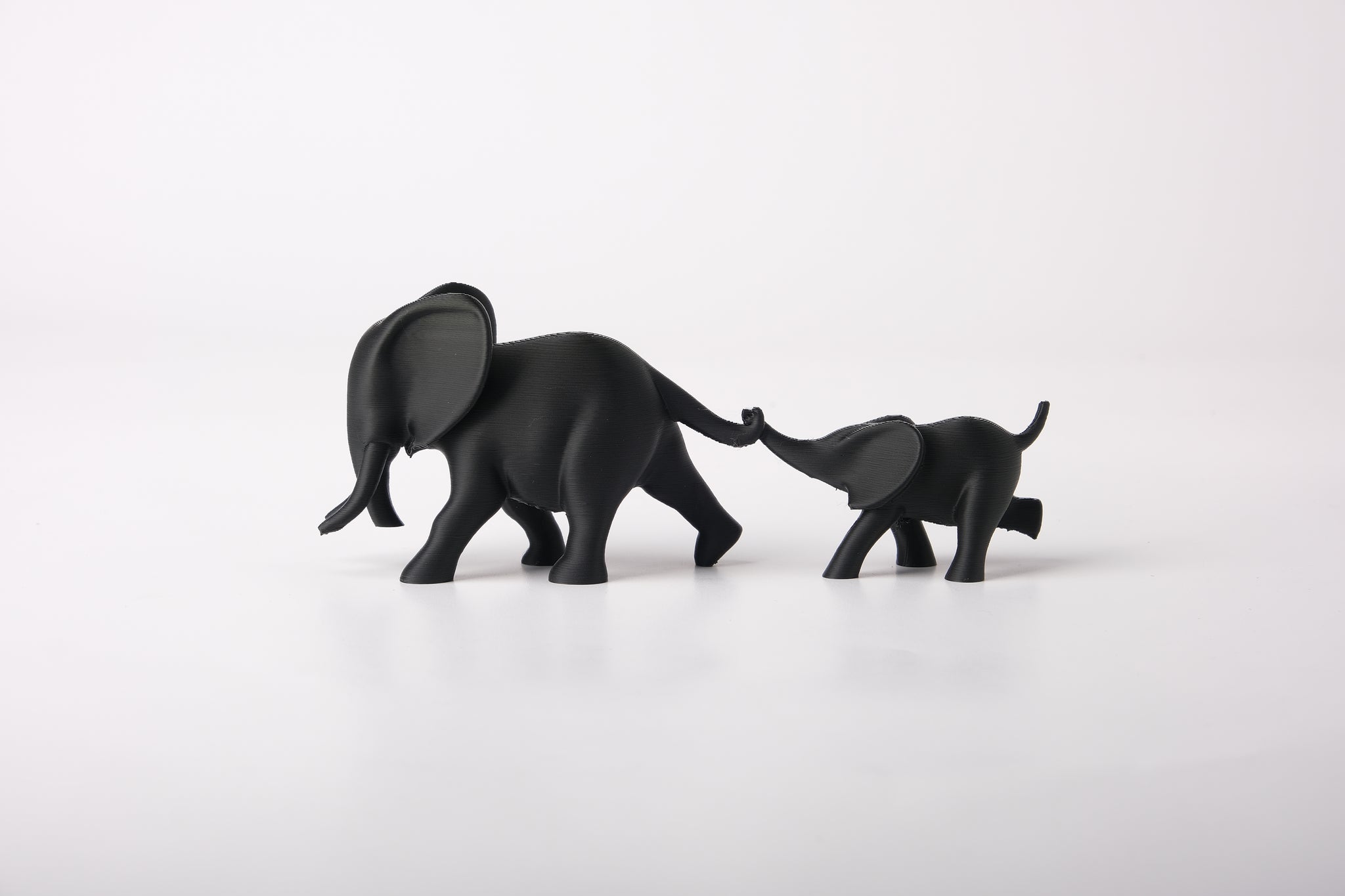 Elephant duo sculpture styled on a wooden shelf next to a small plant and neutral ceramic vase